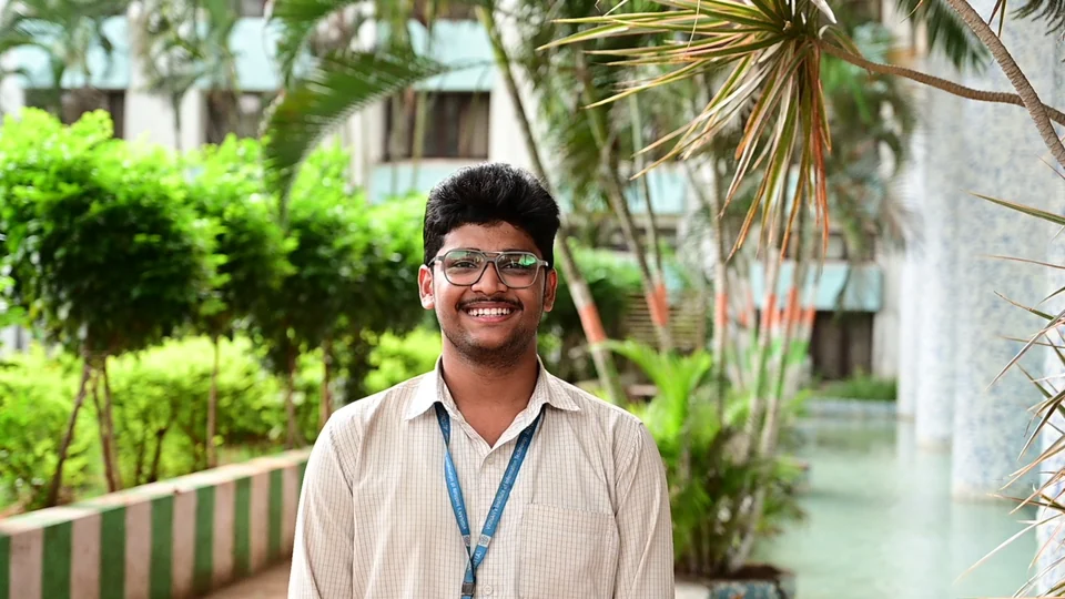 Eshaq smiling outdoors among the trees